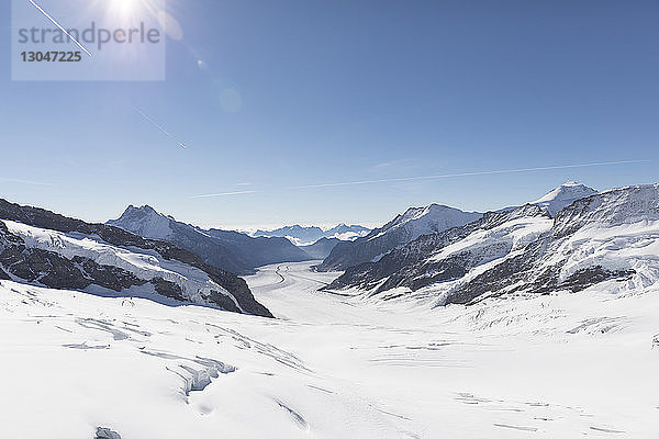 Szenenansicht einer schneebedeckten Landschaft vor blauem Himmel bei sonnigem Wetter