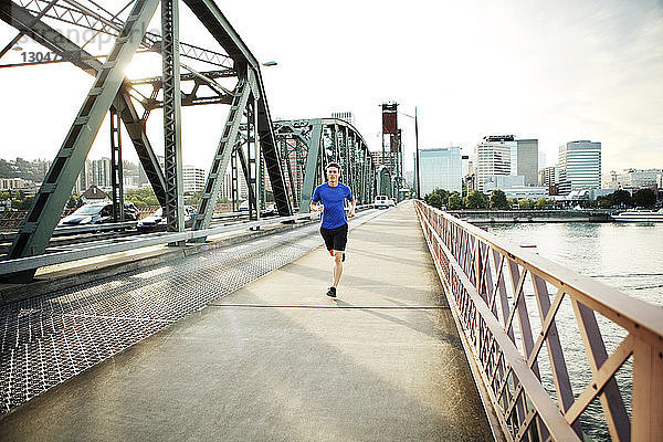 Sportlicher Mann joggt auf Brücke gegen den Himmel