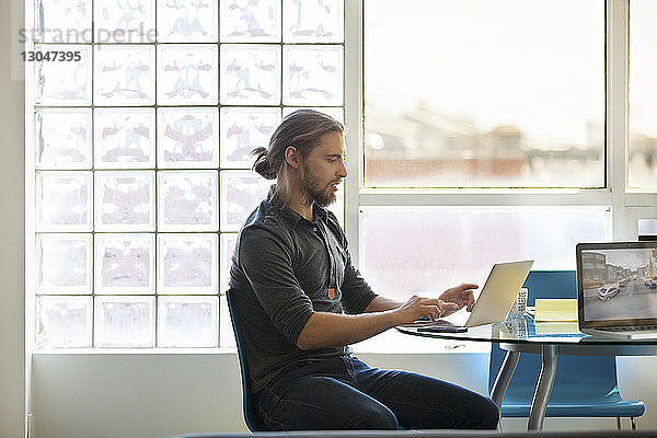 Geschäftsmann mit Laptop auf Tisch gegen Fenster im Kreativbüro