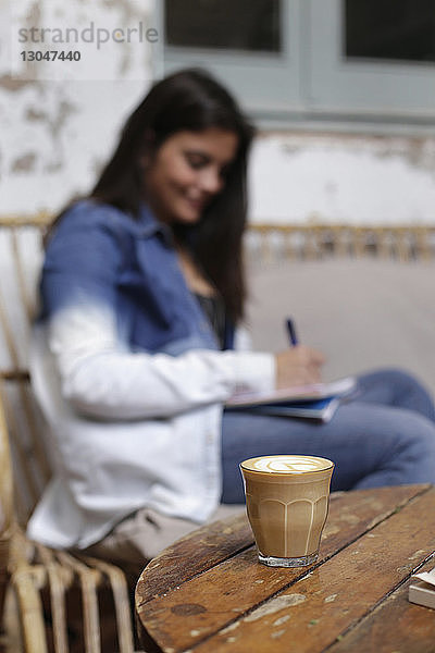 Schreibende Frau mit Kaffee auf dem Tisch im Vordergrund