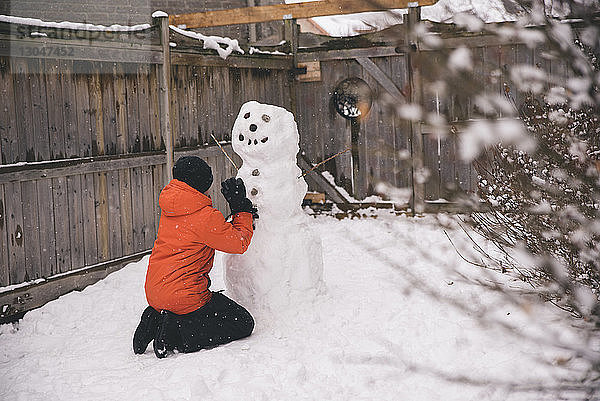 Seitenansicht eines Jungen  der im Hof einen Schneemann baut