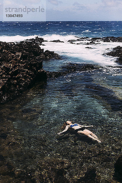 Hochwinkelaufnahme einer Frau  die an einem sonnigen Tag im Meer schwimmt