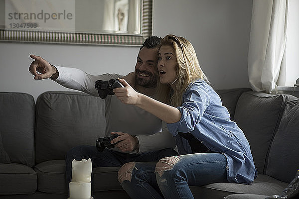 Glückliches Paar spielt Videospiel  während es zu Hause auf dem Sofa sitzt