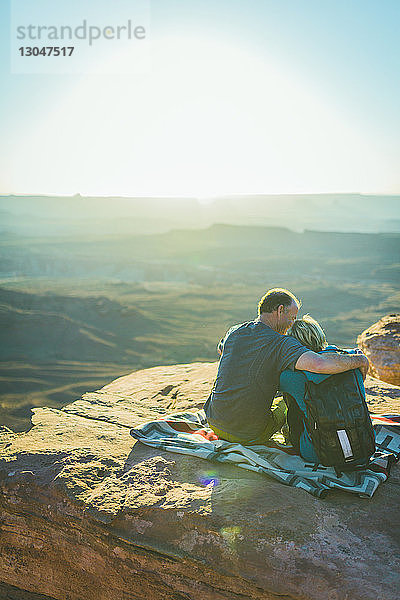 Rückansicht eines romantischen Paares  das an einem sonnigen Tag im Canyonlands-Nationalpark auf einem Berg sitzt