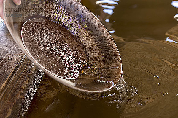 Gekrümmte Hand eines Mannes  der Wasser aus einer rostigen Metallschüssel gießt