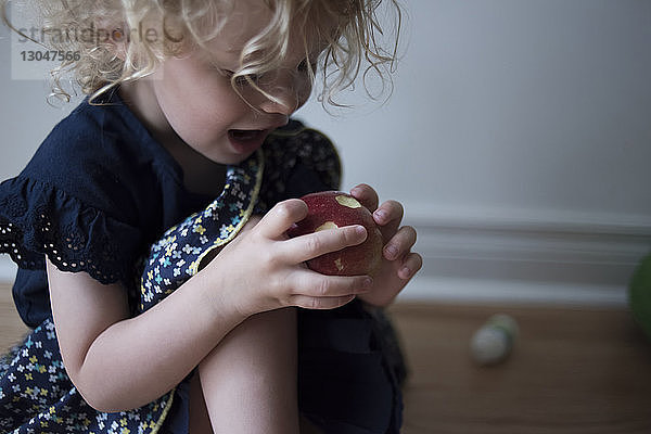 Glückliches Mädchen schaut auf den Apfel  während es zu Hause auf dem Boden sitzt
