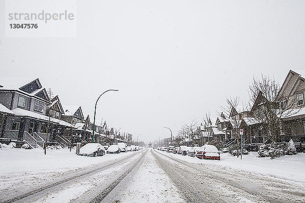 Schneebedeckte Straße inmitten von Häusern gegen klaren Himmel im Winter