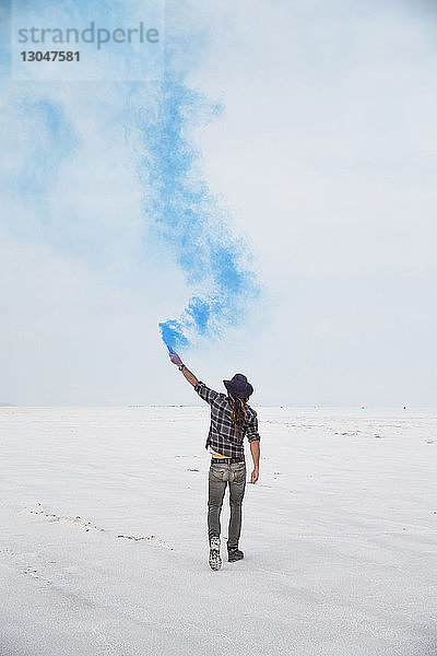 Rückansicht eines Mannes  der eine Rauchbombe hält  während er auf Bonneville Salt Flats gegen den Himmel steht