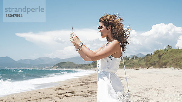 Seitenansicht einer Frau  die im Sommer am Ufer stehend mit einem Smartphone fotografiert