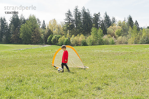 Junge spielt bei Sonnenschein Fussball auf Rasen