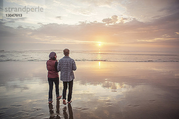 Rückansicht eines Paares  das bei Sonnenuntergang am Strand gegen den Himmel läuft