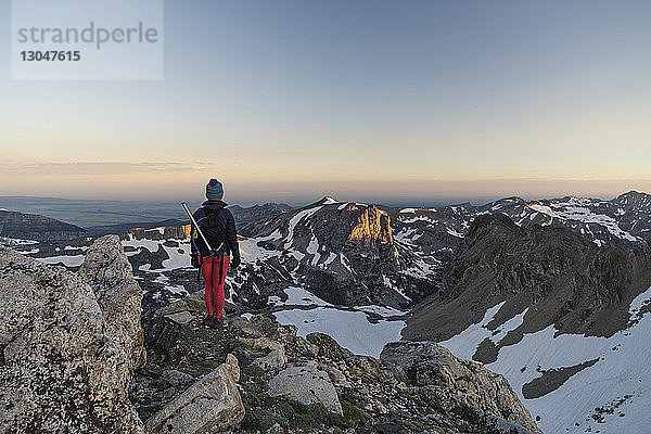 Rückansicht eines Wanderers  der bei Sonnenuntergang auf einem Berg gegen den Himmel steht