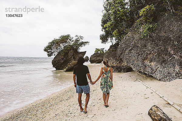 Rückansicht eines Paares  das sich beim Strandspaziergang an den Händen hält