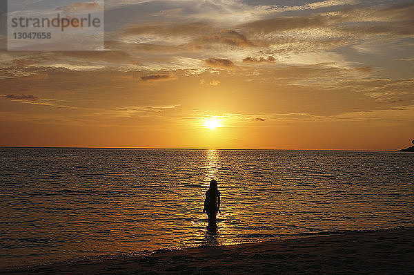 Rückansicht einer Silhouettenfrau  die bei Sonnenuntergang im Meer gegen den Himmel steht