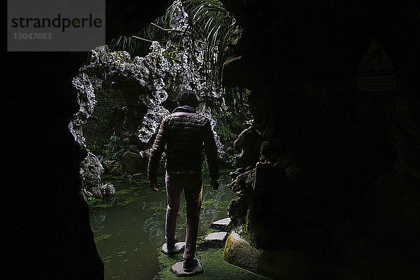 Rückansicht eines auf Trittsteinen gehenden Menschen in einer Höhle