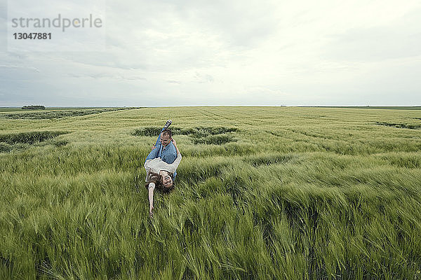 Mann trägt unbekümmerte Frau  während er im Grasfeld gegen den Himmel steht