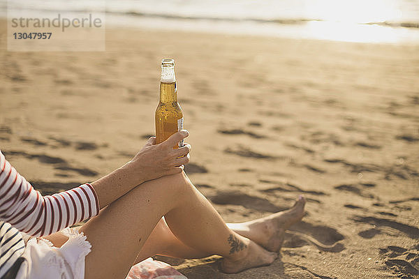 Niedriger Teil einer Frau  die beim Entspannen am Strand eine Bierflasche hält