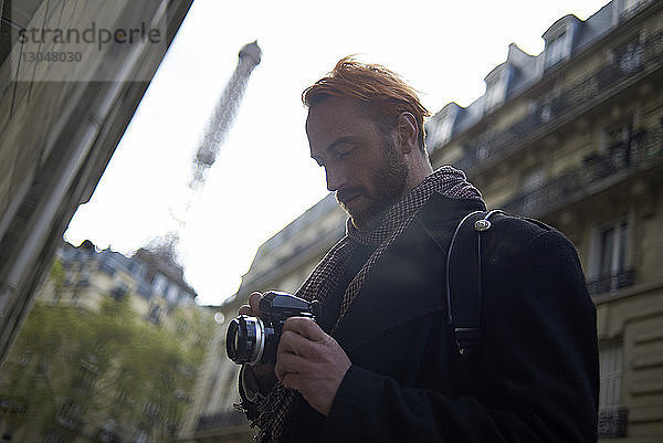 Niedrigwinkelansicht eines Mannes  der mit einer DSLR-Kamera Bilder gegen den Eiffelturm und Gebäude betrachtet