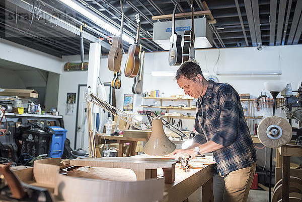 Arbeiter beim Gitarrenbau  während er in der Werkstatt an der Werkbank steht