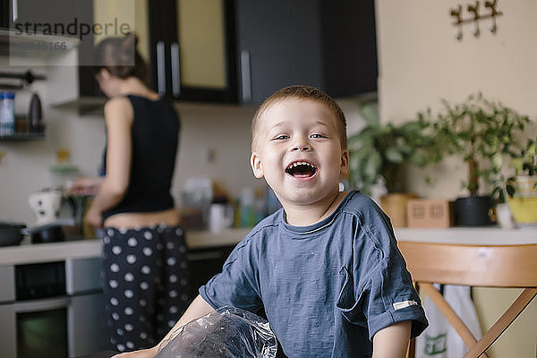 Porträt eines glücklichen Jungen mit einer Mutter  die zu Hause im Hintergrund arbeitet