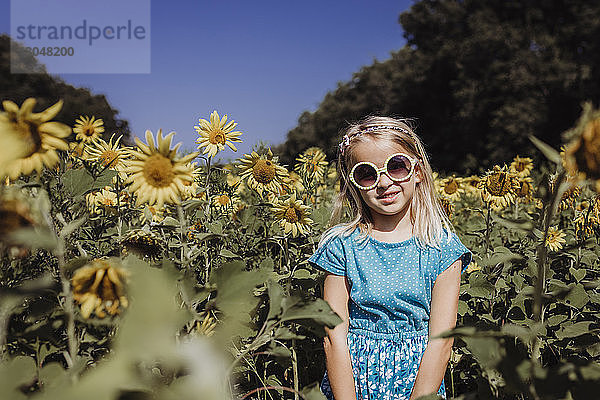 Porträt eines Mädchens mit Sonnenbrille  das im Sommer auf einem Sonnenblumenfeld steht