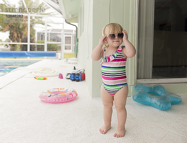 Mädchen in Badebekleidung trägt eine Sonnenbrille in Herzform  während sie am Poolrand steht