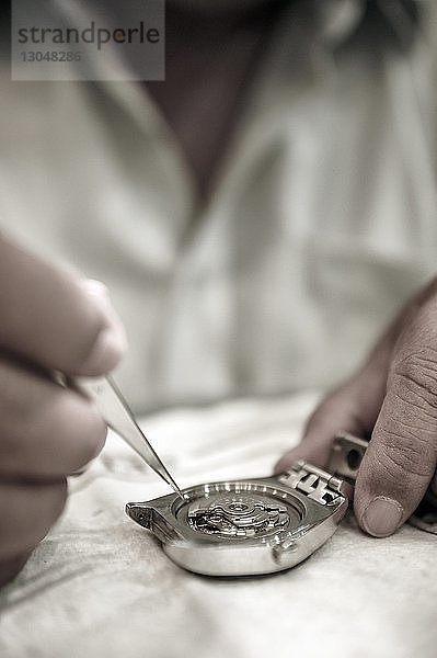 Mittelteil eines Mannes  der eine Uhr auf einem Tisch in einer Werkstatt repariert