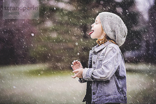 Seitenansicht eines Mädchens mit herausgestreckter Zunge  das bei Schneefall im Park steht