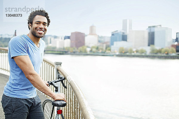 Porträt eines auf einer Brücke stehenden männlichen Athleten mit Fahrrad am Fluss