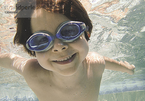 Porträt eines hemdlos lächelnden Jungen  der im Schwimmbad unter Wasser schwimmt