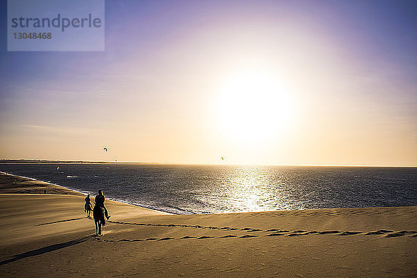 Silhouette von Menschen  die am Strand am Ufer vor dramatischem Himmel reiten