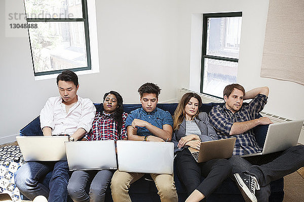 Müde Geschäftsleute  die im Büro auf dem Sofa liegend einen Laptop benutzen