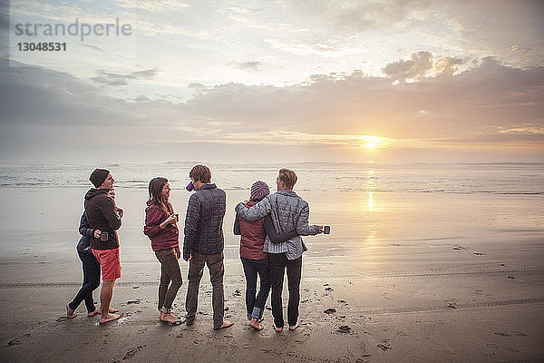 Paare  die bei Sonnenuntergang am Strand am Ufer stehen