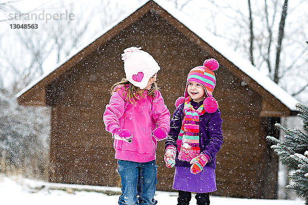 Glückliche Schwestern spielen mit Schnee  während sie bei Schneefall im Freien stehen