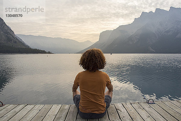 Wanderer schaut auf Aussicht  während er auf dem Steg über dem Minnewanka-See vor Bergen sitzt