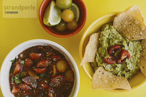 Draufsicht auf Salsa und Guacamole  serviert mit Zutaten auf gelbem Hintergrund