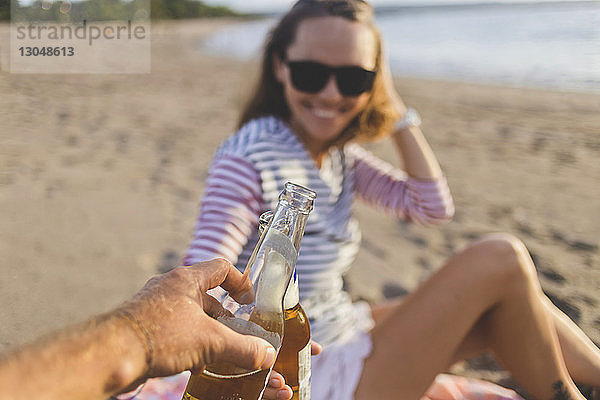 Abgehackte Hand eines Mannes  der mit einem Freund am Strand auf Bier anstößt