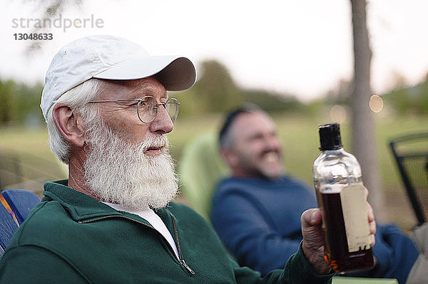 Mann hält Flasche  während er mit einem Freund im Hof sitzt
