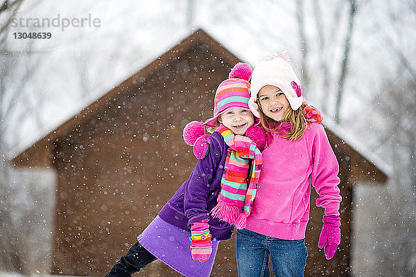 Porträt von glücklichen Schwestern  die bei Schneefall im Freien stehen