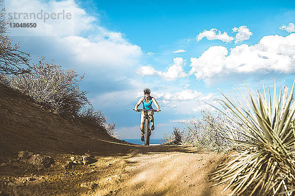 Mountainbike fahrende Radfahrerin auf Feldweg gegen bewölkten Himmel