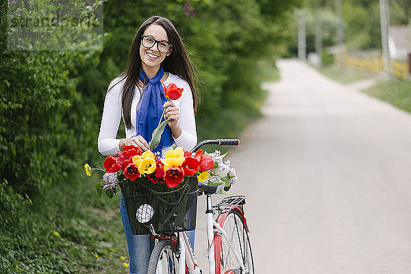 Porträt einer fröhlichen jungen Frau mit Fahrrad  die eine Tulpe auf der Strasse hält