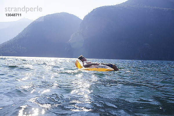 Seitenansicht eines Mannes  der im Sommer auf einem Floß im See vor den Bergen liegt