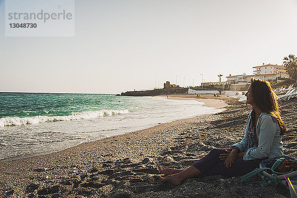 Nachdenkliche Frau sitzt am Strand und schaut auf die Aussicht
