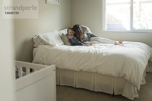 Mutter küsst Sohn  während sie zu Hause auf dem Bett sitzt