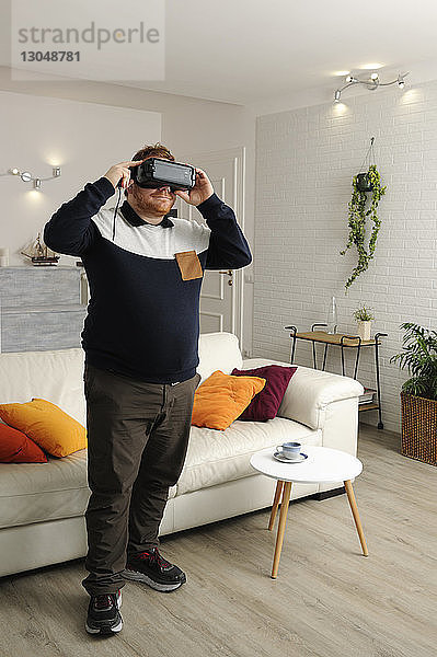Mann schaut zu Hause durch einen Virtual-Reality-Simulator  während er zu Hause steht