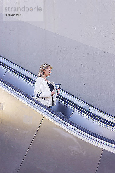 Geschäftsfrau steht auf Rolltreppe an Mauer in der Stadt