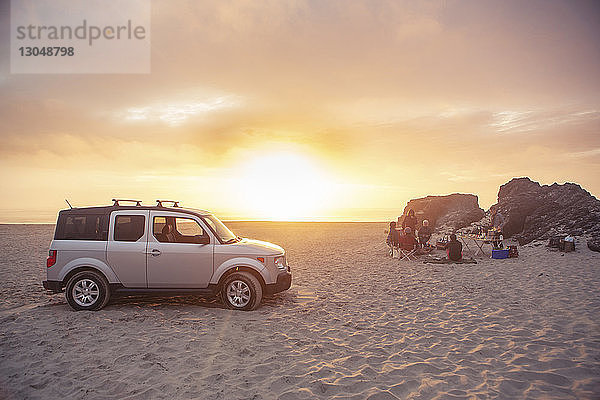Geländewagen am Strand geparkt  während Freunde bei Sonnenuntergang zelten