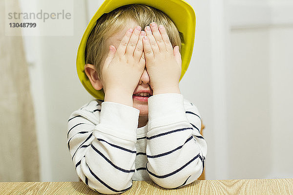 Verspielter Junge  der beim Spielen zu Hause die Augen mit den Händen bedeckt