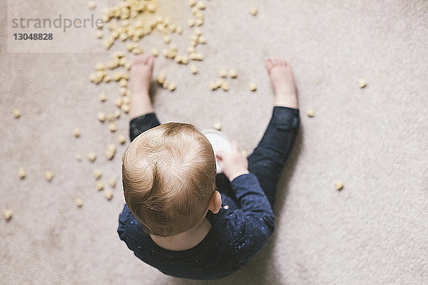 Draufsicht eines Kleinkindes  das auf dem Boden sitzend Nahrung isst