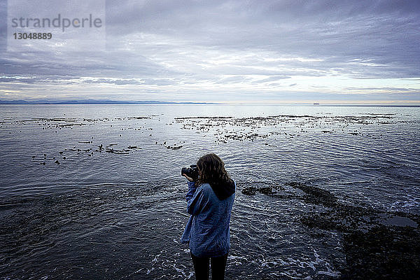 Rückansicht einer Frau  die an der Küste am Strand stehend fotografiert
